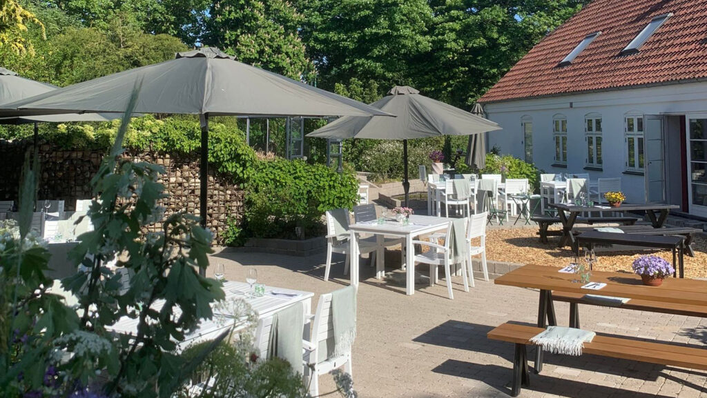 Hyggelig gårdhave med dækkede borde og parasoller på Essens Gaarden, restaurant i Nordjylland.